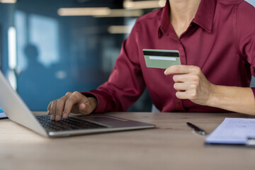 Woman holding a credit card and typing on a laptop keyboard, engaged in secure online shopping, e-commerce, and digital banking transactions from a modern office environment