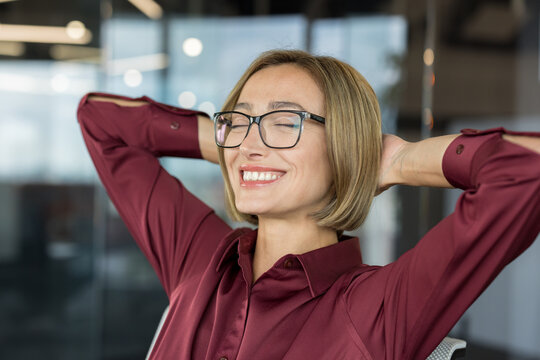 Happy businesswoman relaxing with hands behind head, smiling confidently and feeling satisfied during a break in a modern office, representing work-life balance and job satisfaction