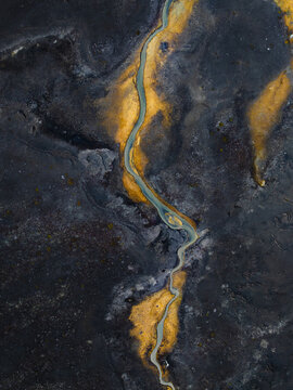Aerial view of a sinuous river cutting through a landscape of contrasting yellows and blacks, creating a striking geothermal tableau, Geothermal Areas, Iceland.