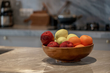 Wooden bowl filled with apples, lemons, and oranges on a grey marble kitchen countertop.