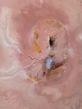 Aerial view of a surreal landscape of pink hues and swirling patterns punctuated by dark voids and delicate fractures, Geothermal Areas, Iceland.
