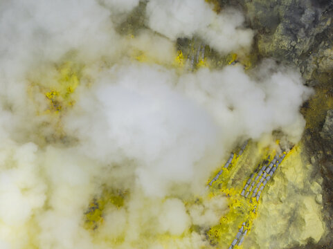 Aerial view of ethereal clouds swirling amidst the yellow sulfur deposits of Mount Ijen's volcanic landscape, East Java, Indonesia.