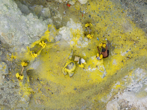 Aerial view of sulphur miners carrying heavy loads of bright yellow sulphur across the volcanic landscape, Mount Ijen, East Java, Indonesia.