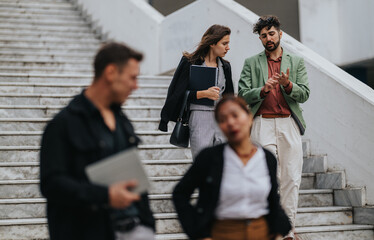 Fototapeta premium A group of coworkers in smart casual attire discuss ideas on a marble staircase, with notebooks and folders in hand.