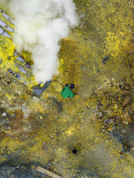 Aerial view of a lone figure amidst the sulphur mines and billowing smoke, the earth painted in vibrant yellows and browns, Mount Ijen, East Java, Indonesia.