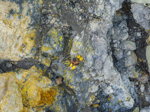 Aerial view of a textured tapestry of rocks and minerals painted with strokes of yellow and grey, creating a surreal landscape, Mount Ijen, East Java, Indonesia.