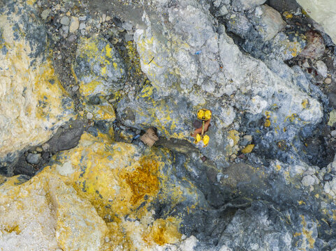 Aerial view of the rugged, mineral-rich terrain displaying a tapestry of gold, grey, and sulfurous yellow, Mount Ijen, East Java, Indonesia.