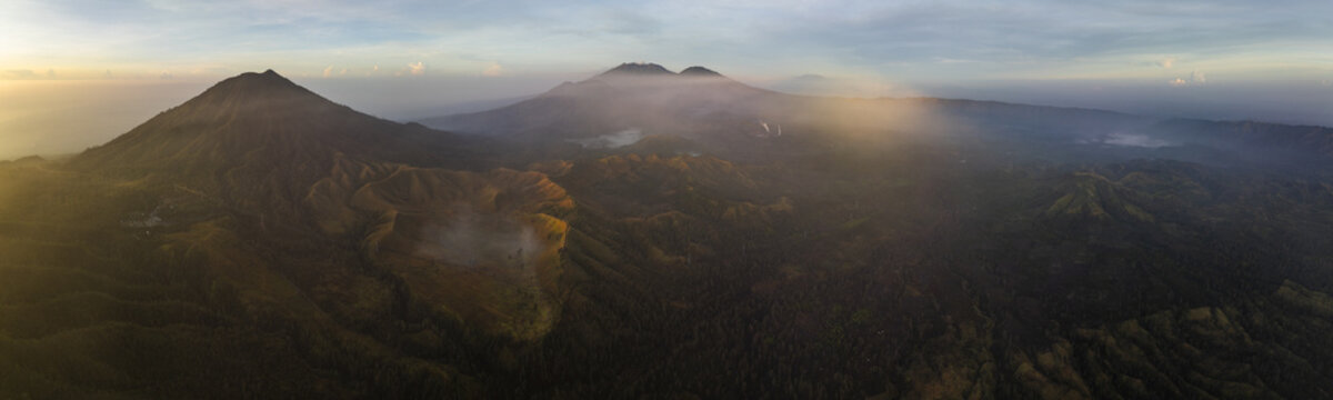 Aerial view of the majestic Mount Ijen's volcanic landscape, where golden light kisses the caldera's rim amidst the dense forest, Mount Ijen, East Java, Indonesia.