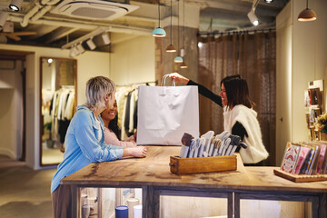 Shop assistant handing shopping bag to smiling customers in boutique