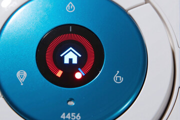 Macro close-up of a round, blue smart home thermostat's digital dial showing a red glowing indicator for heating control