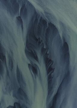 Aerial view of glacial rivers weaving intricate patterns across volcanic sands, creating a surreal landscape of icy blues and earthy browns, South Coast, Iceland.