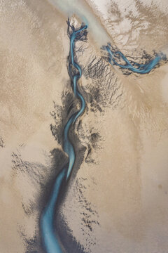 Aerial view of a braided river carves through the stark, sandy landscape, its turquoise waters creating a mesmerizing contrast, South Coast, Iceland.