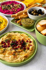 A vibrant spread showcases different types of hummus including classic, beetroot, broccoli, and turmeric. Accompanied by olives and breadsticks, it invites sharing and enjoyment