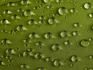 Water drops on waterproof membrane fabric. Detail view of texture of green waterproof cloth.