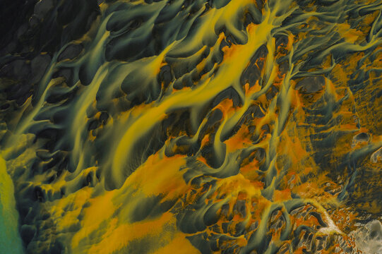 Aerial view of braided rivers paint the landscape with veins of ochre and teal, contrasting against the dark earth, South Coast, Iceland.