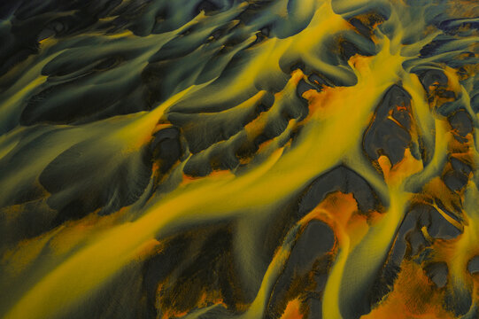 Aerial view of braided river streams carve through the landscape with striking yellow hues against dark earth tones, South Coast, Iceland.