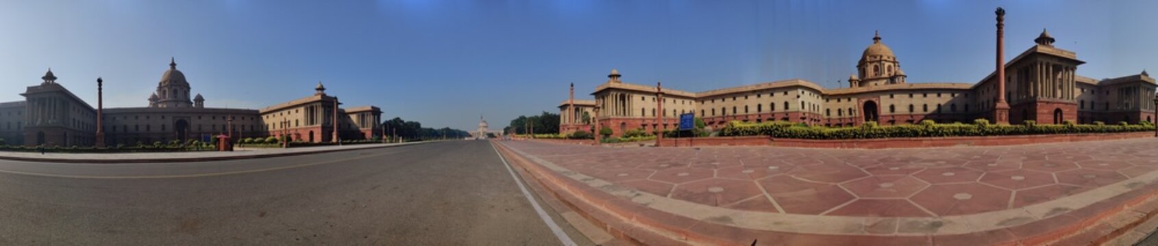 Panoramic view of the Secretariat Buildings and Rashtrapati Bhavan in New Delhi, showcasing grand colonial architecture, wide roads, stone pathways, and a clear blue sky.
