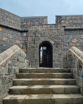 Stone steps leading to an old arched entrance at Worli Fort in Mumbai, India. The historic structure features weathered stone walls and traditional coastal fort architecture.
