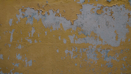 Close-up of an old concrete wall with yellow paint peeling and cracking, revealing faded grey plaster underneath. Weathered and aged surface ideal for use as grunge, urban decay