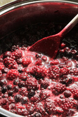 Fresh berries and fruit simmering in pan for homemade jam, sweet healthy cooking with wooden spoon. Vertical portrait photo.