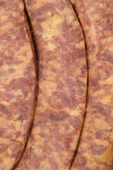 An extreme close-up, full frame shot of three raw sausages, highlighting the rough texture and marbling of the uncooked meat filling