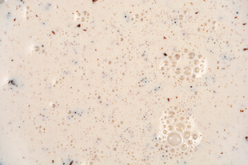 An extreme close-up, full frame shot of sweet cream liquid mixed with tiny chocolate particles and small surface bubbles