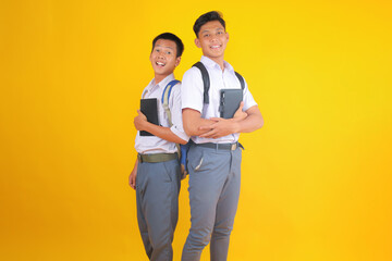 Cheerful Students Pose Back to Back With Notebooks in Vibrant Yellow Studio Portrait