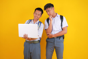 Excited Students Collaborating on Laptop Project in Front of Vibrant Yellow Background