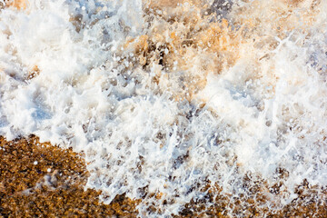 texture of sea foam on the sandy beach. scenic aqua splash. closeup natural abstract background on a sunny day. summer vacation season. frozen moment of salt water meets golden sand and make art mess