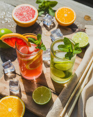 Fototapeta premium Refreshing Summer Citrus Mocktails with Ice and Fresh Mint on Stone Surface 