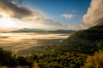 A mountain valley in the morning, with the Autumn sun breaking through the clouds to cast its light, bathing the valley mist in gold colour.