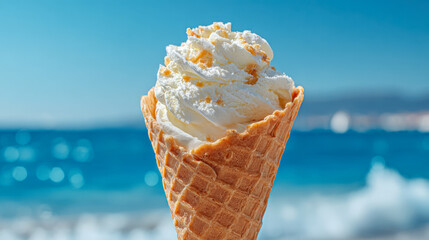 Creamy vanilla soft serve ice cream in a crisp waffle cone with a blurred ocean and bright blue sky background on a sunny summer day at the beach