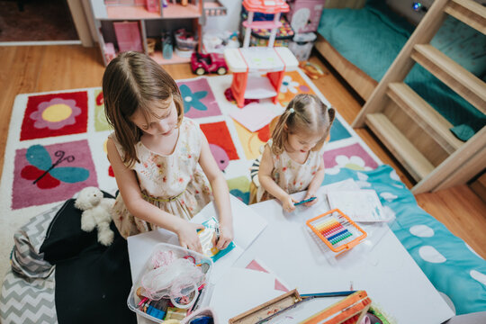 Two young girls are exploring creativity with art supplies in a vibrant children's playroom. The warm and cheerful setting enhances their imaginative hobbies, emphasizing family bonding and artistic