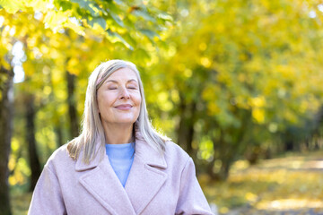 Senior woman relaxing with eyes closed and a gentle smile, feeling the sun on her face in an autumn...