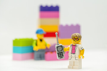 Naklejka premium Lego minifigure businessman with mobile phone standing next to multi-colored bricks. Studio shot.