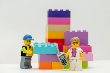 Naklejka premium A miniature LEGO man: A businessman with a mobile phone and a construction worker stand next to LEGO bricks on a white background.