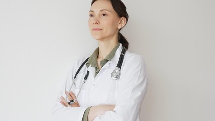Headshot of a doctor woman medical professional in white lab coat, stethoscope draped, standing with crossed arms and displaying confident, authoritative healthcare demeanor. Medicine and health care