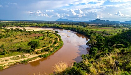 Panoramic vista of a wide, meandering river flowing through a valley, surrounded by lush green fields and distant hills under a cloudy sky