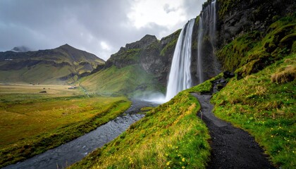 Waterfall with path, and river through green landscape.