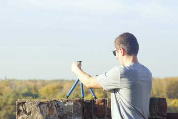 Fototapeta premium Person films himself using a smartphone mounted on a compact travel-friendly tripod in a location with a panoramic view. Symbolizes modern tourism, and exploration-inspired photography practice.