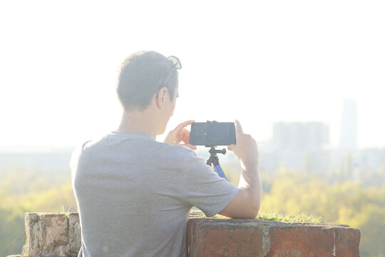 Man recording selfie video on smartphone tripod. Symbolizes organic content creation, self-expression, independence, relaxed communication style, and real-life moments shared with global audience.