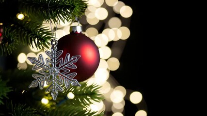Christmas tree branch with red bauble and silver snowflake ornament, festive bokeh lights in dark background. Holiday season celebration and winter decoration background with copy space