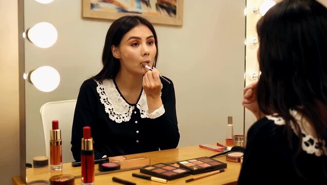 Young woman applying makeup in a well-lit vanity area, with beauty products scattered on the table