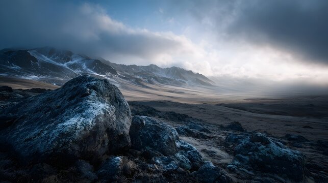 A dramatic vast mountain landscape under a cloudy sky with frost covered foreground rocks and atmospheric mist in the distance - Powered by Adobe
