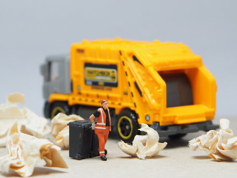 Mini toy of action figure at outdoor with blurred background. Miniature photography concept design. Minifigure of people character with garbage truck at urban city.