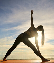 Utthita Trikonasana, Extended Triangle Pose, Yoga on sunset beach on blue cloudy sky background. lady young adult female woman practicing Yoga by the lake Sun salutation Extended triangle pose