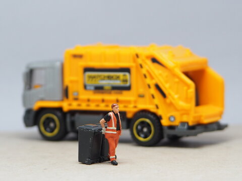 Mini toy of action figure at outdoor with blurred background. Miniature photography concept design. Minifigure of people character with garbage truck at urban city.