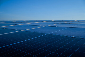 A large solar panel array is seen from above. The panels are blue and are arranged in a grid pattern. The sky is clear and the sun is shining brightly. Concept of clean energy and sustainability