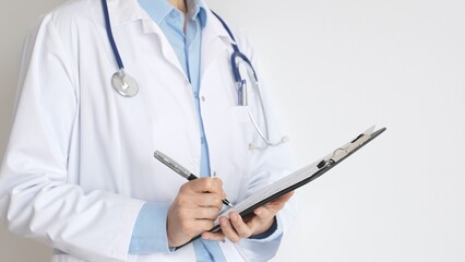 Close up of doctor woman wearing stethoscope and white coat over blue blouse is standing and writing on a black clipboard, representing medical expertise and patient care. Medicine concept