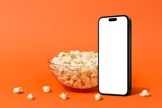 Minimalist smartphone mockup standing beside bowl of popcorn on orange background, ideal for movie night, food branding, or streaming concept imagery
